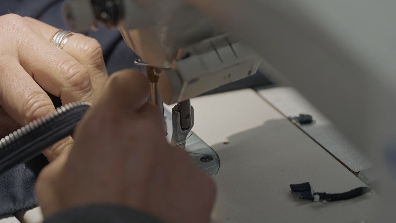 Close up of industrial sewing machine stitching dark fabric while hands guide material