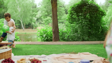 two brothers playing with ball in park. cute sister sitting on blanket outdoors