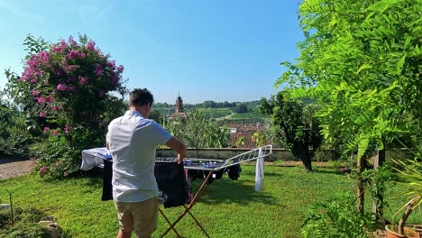 man hangs clothes on rack in sunny garden