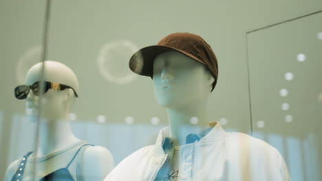 a view of male and female mannequins dressed in stylish outfits in a mall. the male mannequin is wearing a cap and jacket, while the female mannequin sports sunglasses and a trendy top