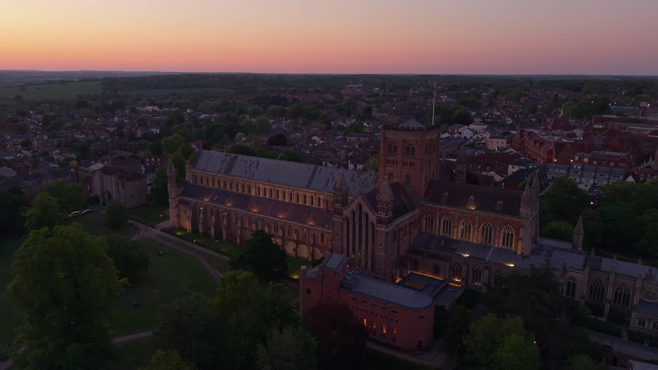 Aerial drone captures the cityscape of St Albans at night, highlighting the illuminated cathedral at the center surrounded by twinkling city lights and evening atmosphere