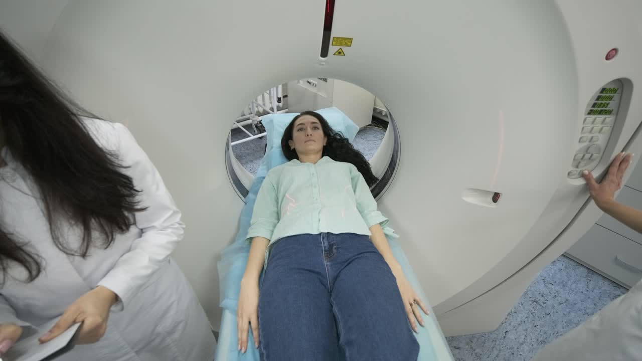 la paciente está siendo sometida a una tomografía computarizada o resonancia magnética bajo la supervisión de dos radiólogos calificados en una clínica médica moderna. la paciente está acostada en una cama de ct o mri, moviéndose dentro de la máquina.