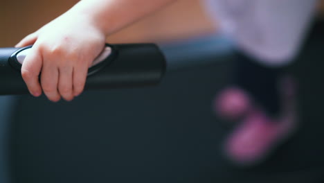 una niña pequeña en zapatillas de deporte camina en una cinta de correr apoyada en el mango