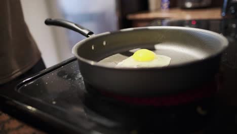 close-up static shot of hands cracking an egg on a non-stick frying pan over an induction stovetop