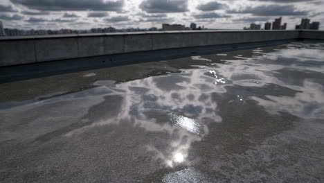 water puddle on rooftop reflecting clouds and cityscape