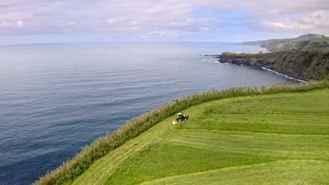 tractor cutting grass in field on steep sea cliff, azores, aerial view