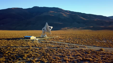 aerial view towards a large satellite dish at a desert - approaching, drone shot