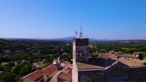 Malerische-Dorfszene:-Glockenturm-Der-Kirche-Mit-Französischer-Flagge-Inmitten-Südfrankreichs,-Im-Hintergrund-Die-Pic-Saint-Loup-Berge