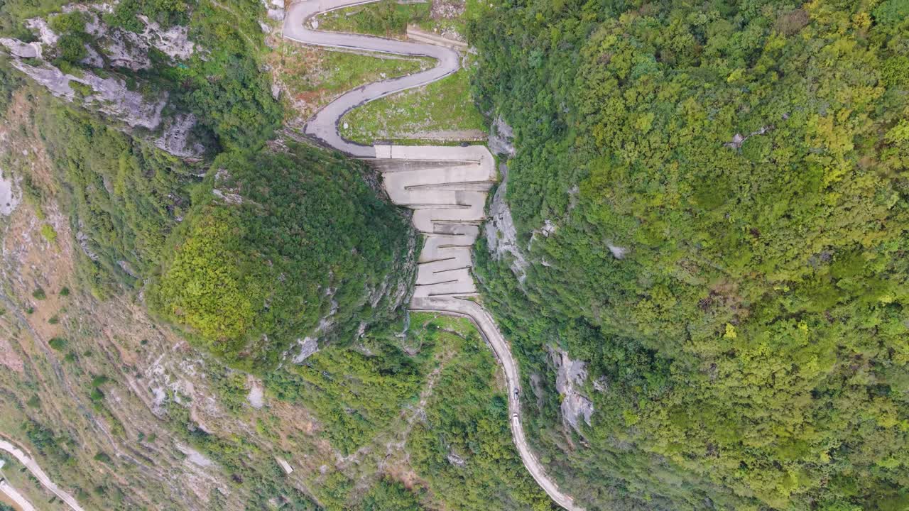 Top-down drone shot of the steep, sheer rock formations and the zigzag road carved into the cliffside at Lingpaishi, Wuxi County, China. Captures remote natural beauty and engineering. UHD