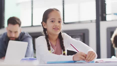 Portrait-of-happy-biracial-schoolgirl-and-schoolchildren-using-laptop-in-school-classroom