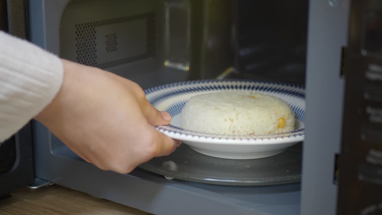 Mano che toglie un piatto di riso cotto dal microonde