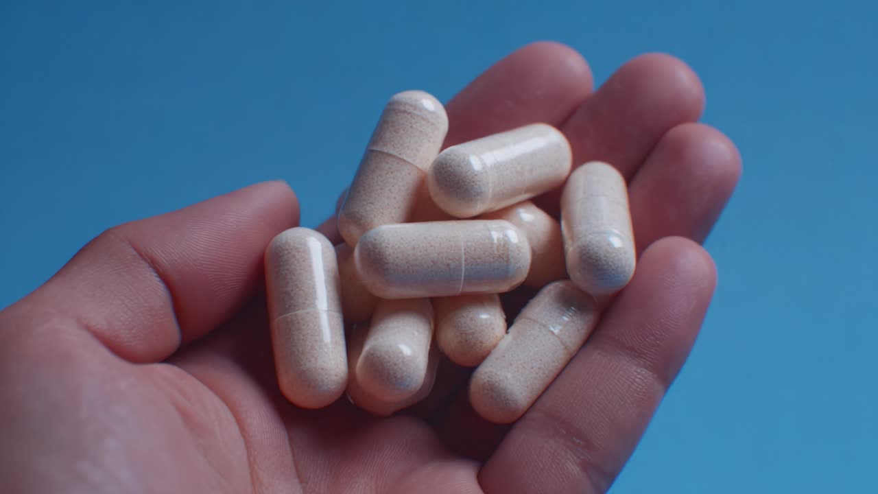 Un puñado de suplementos dietéticos: primer plano de cápsulas de color claro sobre un fondo azul que destaca su forma y textura