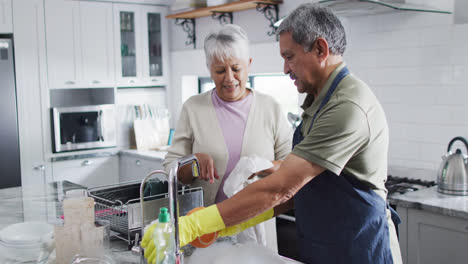 una pareja bi-racial feliz lavando platos en la cocina