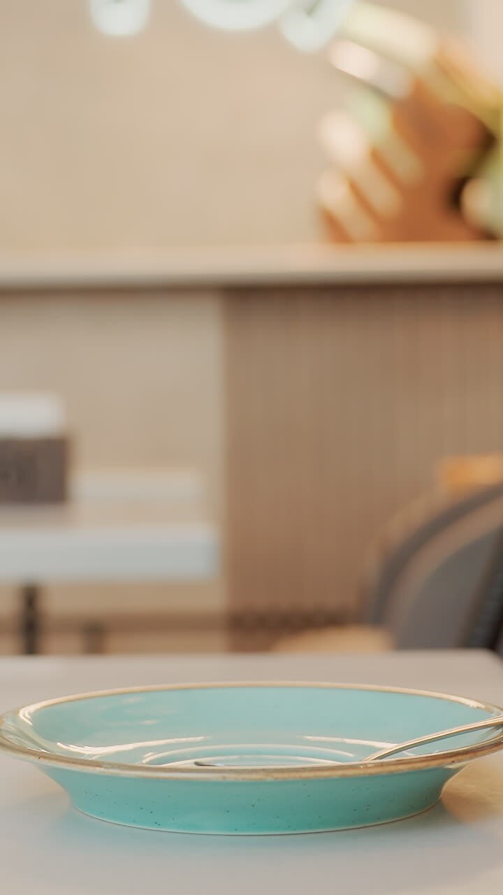 turquoise cup on table caucasian hand lifts saucer placement, ceramic texture, soft sunlight, blurred cafe interior, pastel decor, steam hinting at fresh coffee, relaxed morning ritual, inviting