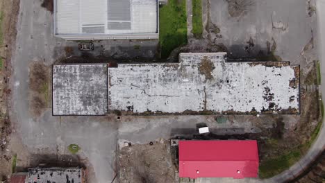 top down aerial drone footage moving left over a large abandoned building with a decaying, overgrown roof