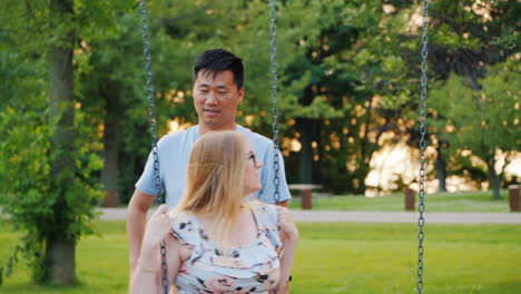 multi-ethnic couple - asian man and pregnant caucasian woman ride on a swing happy young family