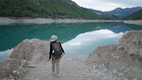 woman hiking by a turquoise lake in a mountainous region