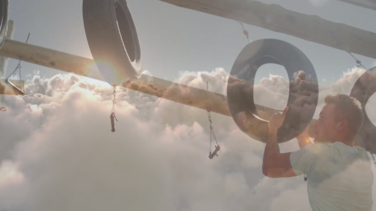 Climbing tire obstacle, man reaching for sunlight streaming through clouds