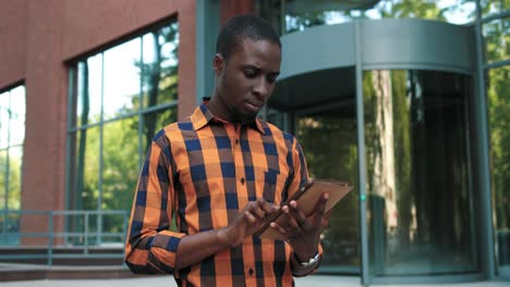 camera zooming on african american man using a tablet while preparing to exams during the break near the college