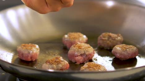 chief checks small size juicy meat balls frying in a steel pan, handheld close up shot