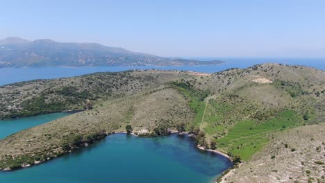 drone view in albania flying over blue sea sorrunded by green landscape hills with mountains on the back