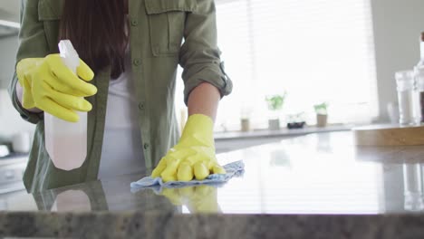 caucasian woman wearing rubber gloves and cleaning table at home