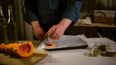 Man-putting-pumpkin-slices-on-baking-sheet.-Pumpkin-pieces-baking-process