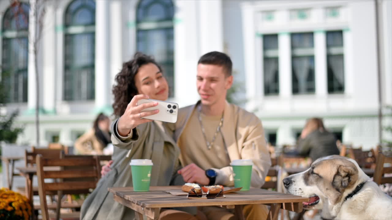 Una coppia felice all'aperto vicino a un bar. Scattano un selfie, caffè sul tavolo. Atmosfera autunnale. Movimento al rallentatore