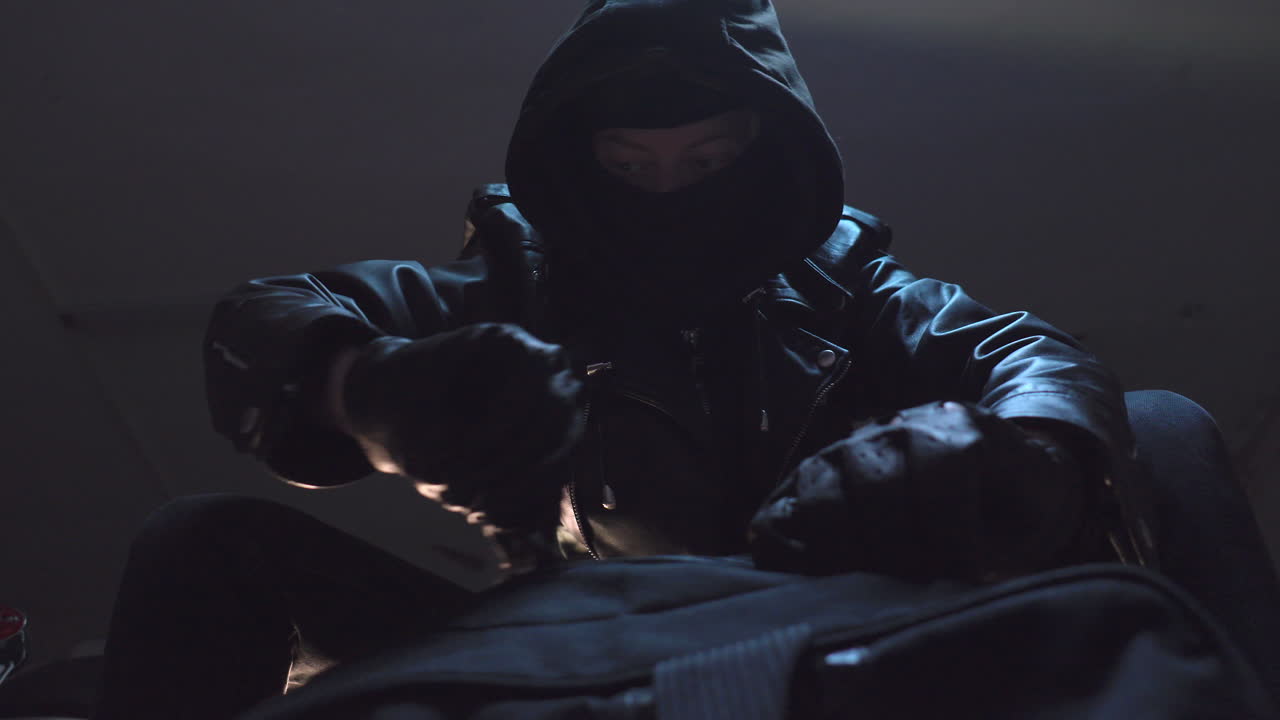 산적 가면을 쓰고 검은 가죽 장갑을 낀 범인이 가방을 닫고 떠난다