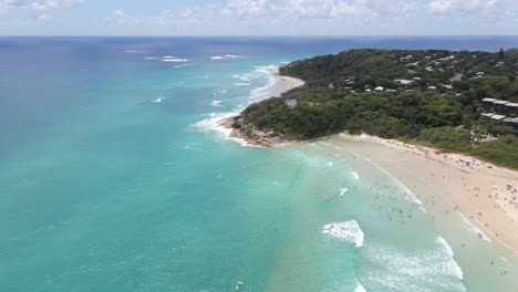 Drone-Fly-Towards-Blue-Beach-With-Tourists-Near-Rocky-Coastal-Cliffs-Of-Cylinder-Headland-Foreshore-In-Point-Lookout,-Australia