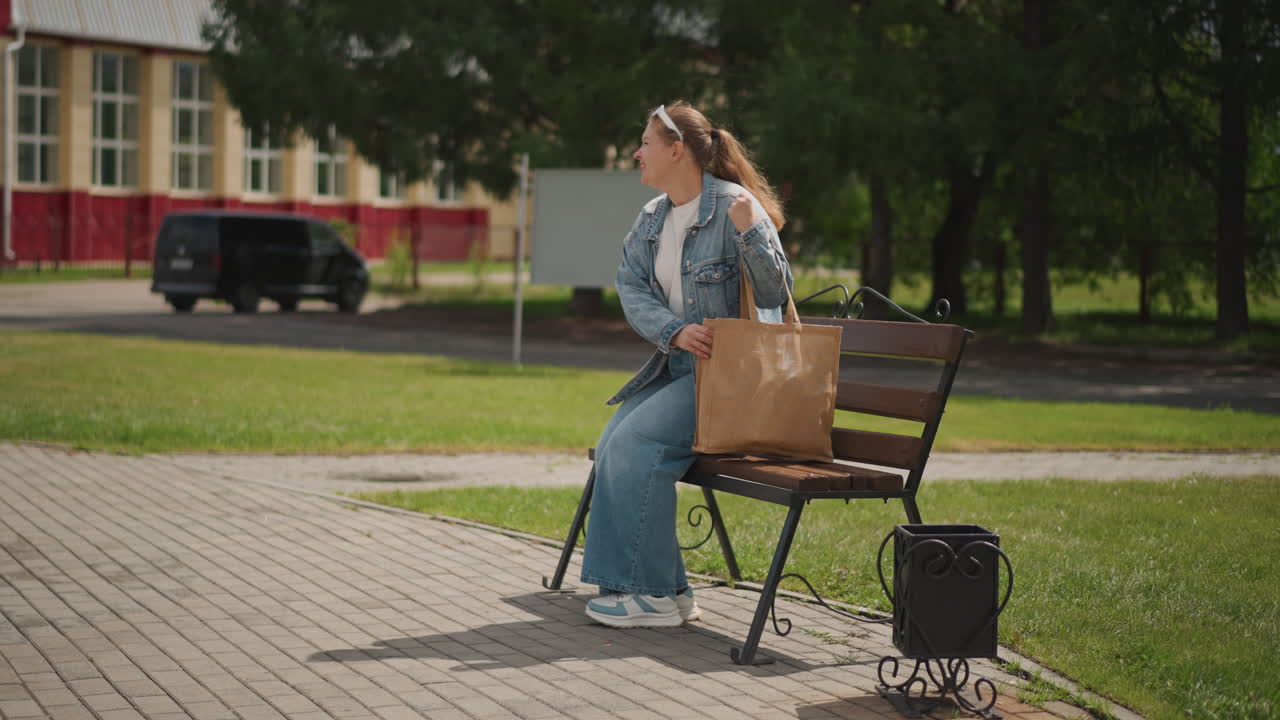 Giovane donna che si rilassa. Donna che si gode un ambiente tranquillo. Giovane donna in denim con cuffie, atmosfera calma. Individuo femminile seduto al sole che indossa abiti casual con accessori