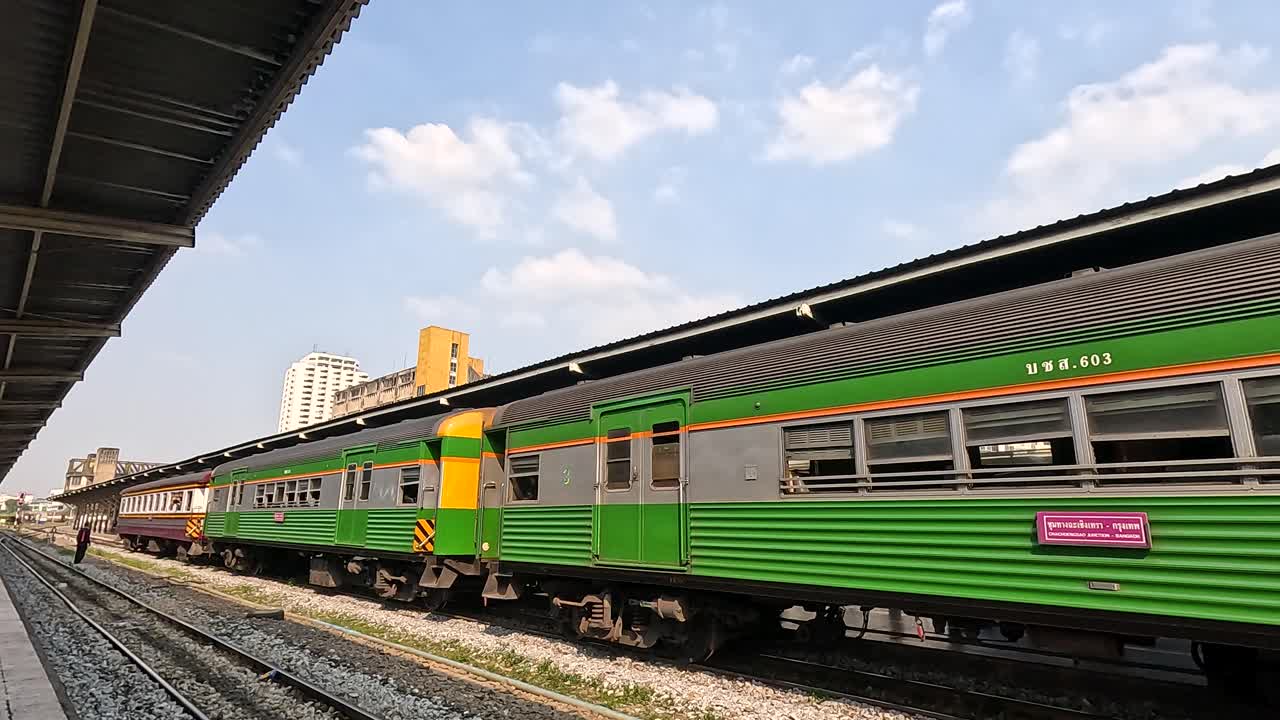 Side view of classic green passenger train slowly departing Bangkok platform under bright daylight