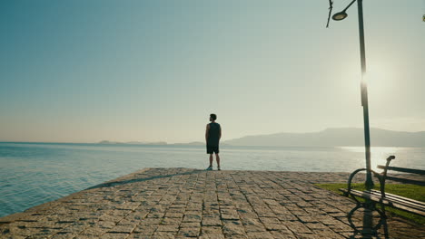 lonely man standing in front of lake watching sunset