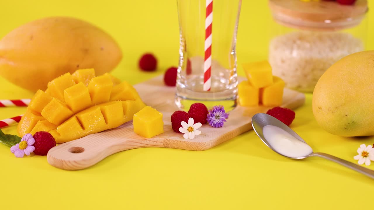 Hand uses spoon to clear mango cubes, raspberries, and flowers from colorful cutting board setup