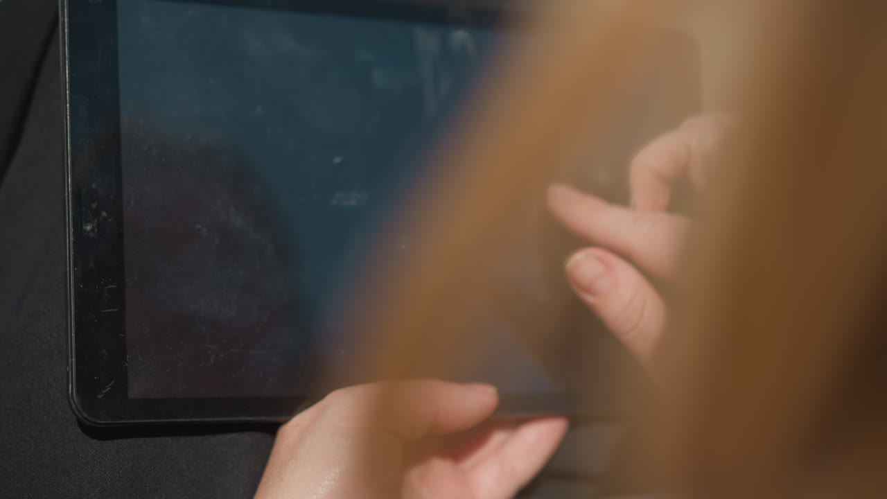 Close up rear view of lady sliding through tablet outdoors under sunlight, reflection of her face visible on glossy screen, symbolizing focus, technology, creativity, digital lifestyle