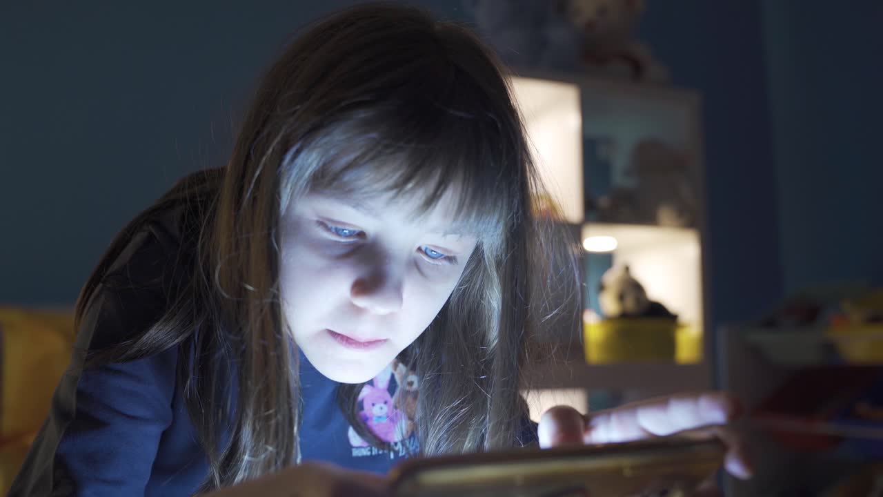 행복한 작은 소녀가 집에서 전화를 보고 있습니다.