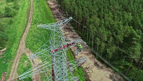 aerial top down of industrial worker in lift crane repairing transmission tower in woodland