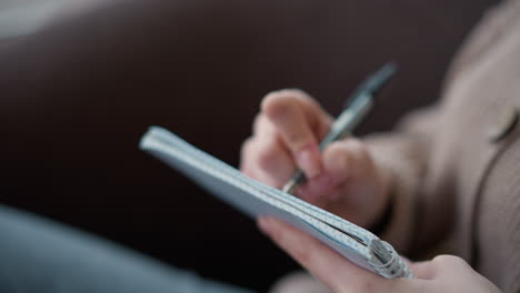 close-up of hand holding a pen and taking notes in a notebook. the focus is on writing while soft background highlights a cozy study environment