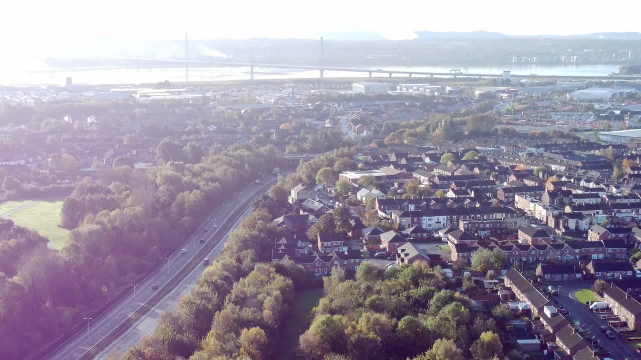 Aerial view looking across countryside dual carriageway traffic country road between woodland treetop at sunrise towards Widnes town
