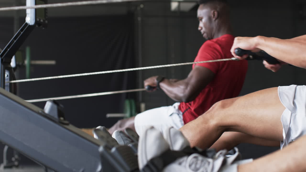 Exercising on rowing machines, men working out together in gym