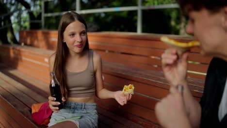 dos jóvenes disfrutando de pizza y refresco en un parque