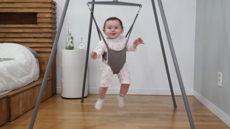 adorable 1-year-old baby jumping in jolly jumper in the room excited