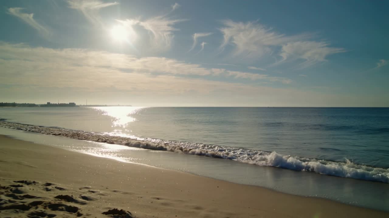 Paisagem marítima com sol baixo a projetar brilho intenso enquanto a ondulação entra, a onda quebra, deixando espuma, para o turismo.