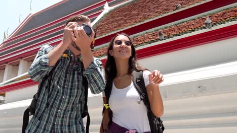 young couple tourist backpackers taking pictures at thai temple in thailand