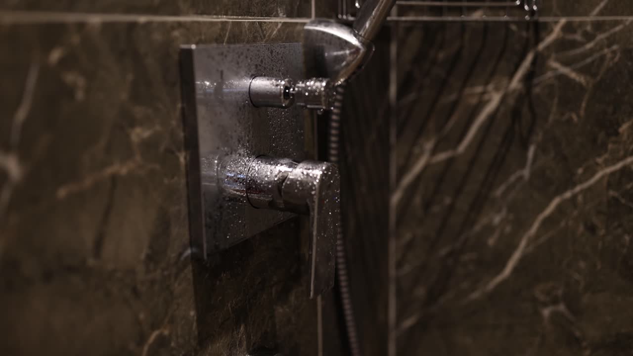 Close-up of a modern shower control with water droplets on a marble wall