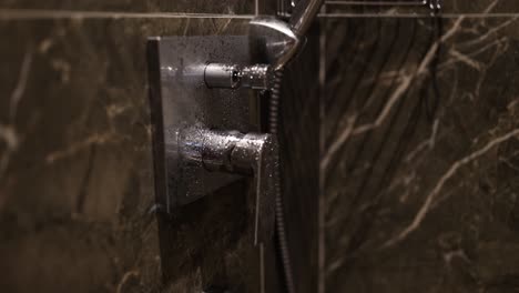 close-up of a modern shower control with water droplets on a marble wall
