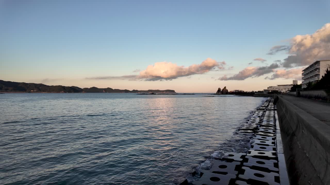 Tranquil scene of Nachi Bay during golden hour, featuring a breakwater wall and serene ocean waters under a sky with soft clouds