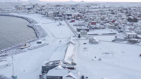 Quiet-coastal-town-on-shore-of-Iceland-covered-in-winter-snow,-aerial