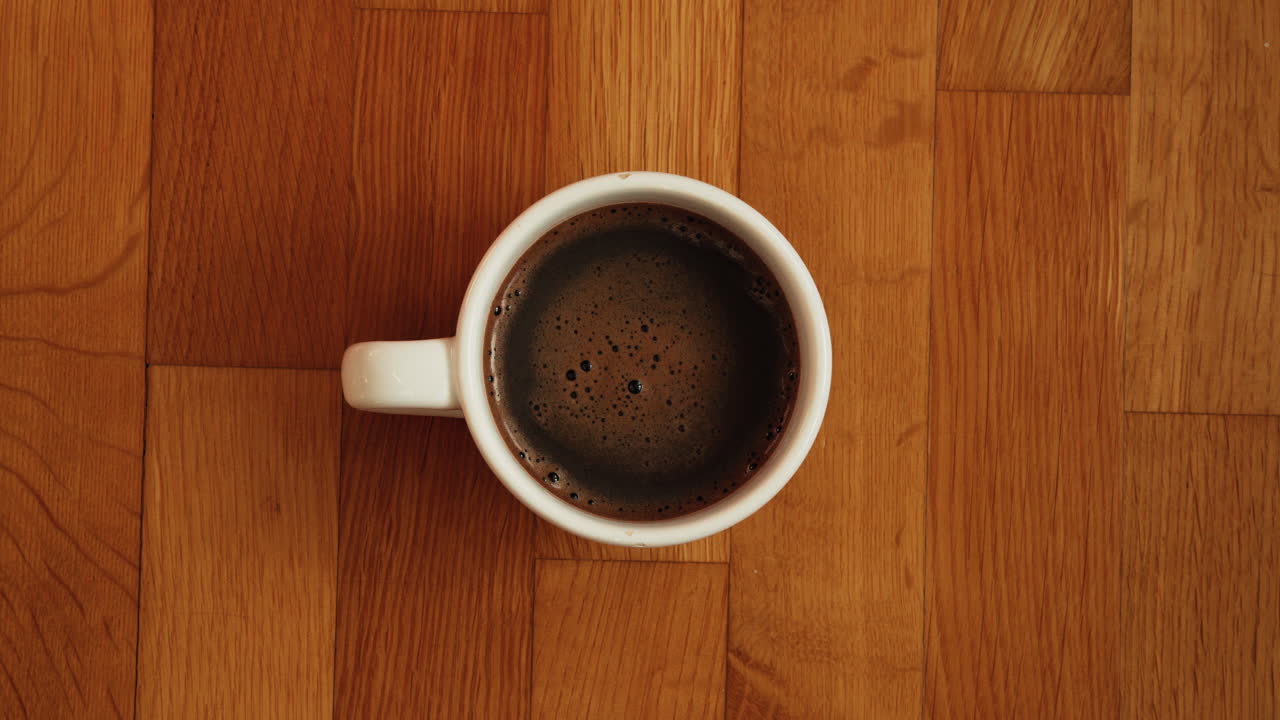 Vista dall'alto di caffè nero appena preparato in una tazza di ceramica bianca posta su una superficie di legno calda. Composizione minimale, atmosfera accogliente e stile di vita quotidiano adatto per le routine mattutine.