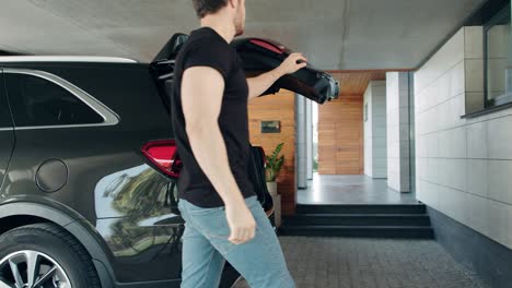 handsome man taking suitcase from car in luxury house. rich man coming home